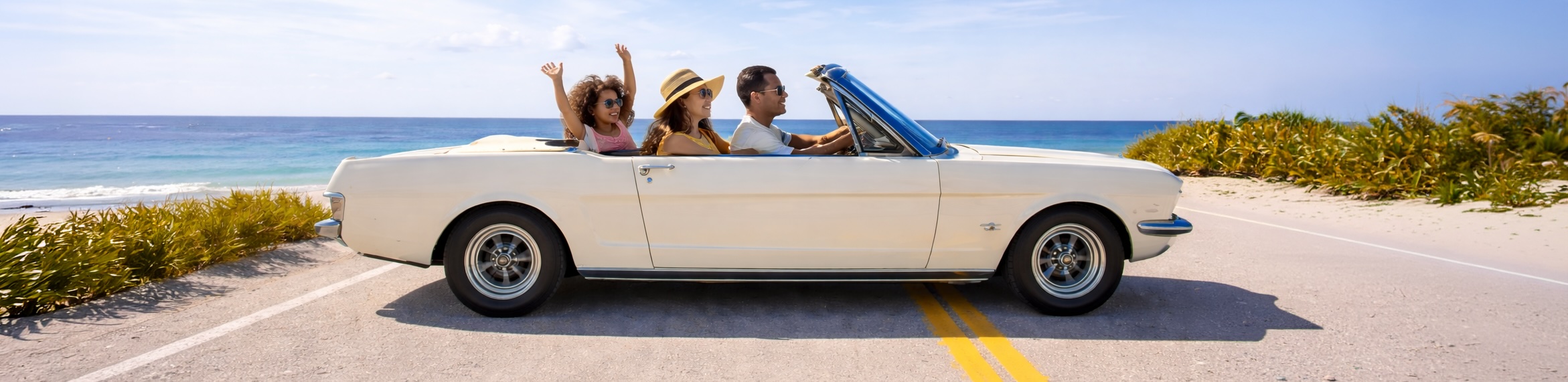 Two women and a man are driving away from the ocean on an old car with two suns shining brightly overhead.